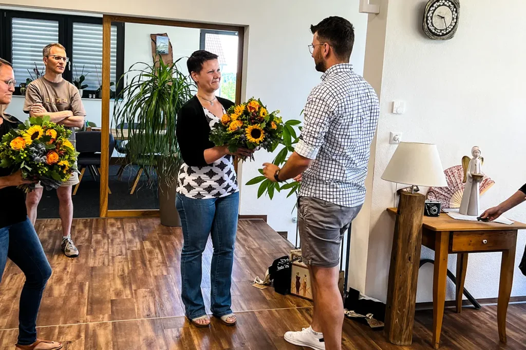 Geschäftsführer Silvan Vogt übergibt Blumenstrauß zum 15. Jubiläum Buchhalterin Barbara Nied
