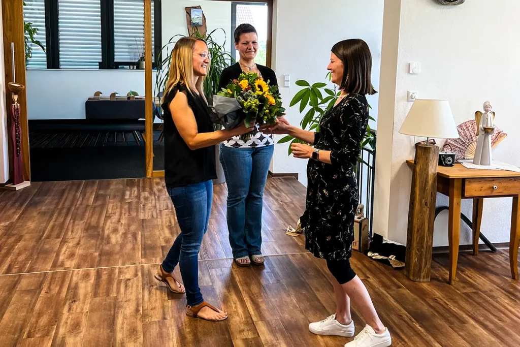 Geschäftsführerin Sarah Vogt übergibt Blumenstrauß zum 15. Jubiläum Reiseplanerin Franziska Häßlein