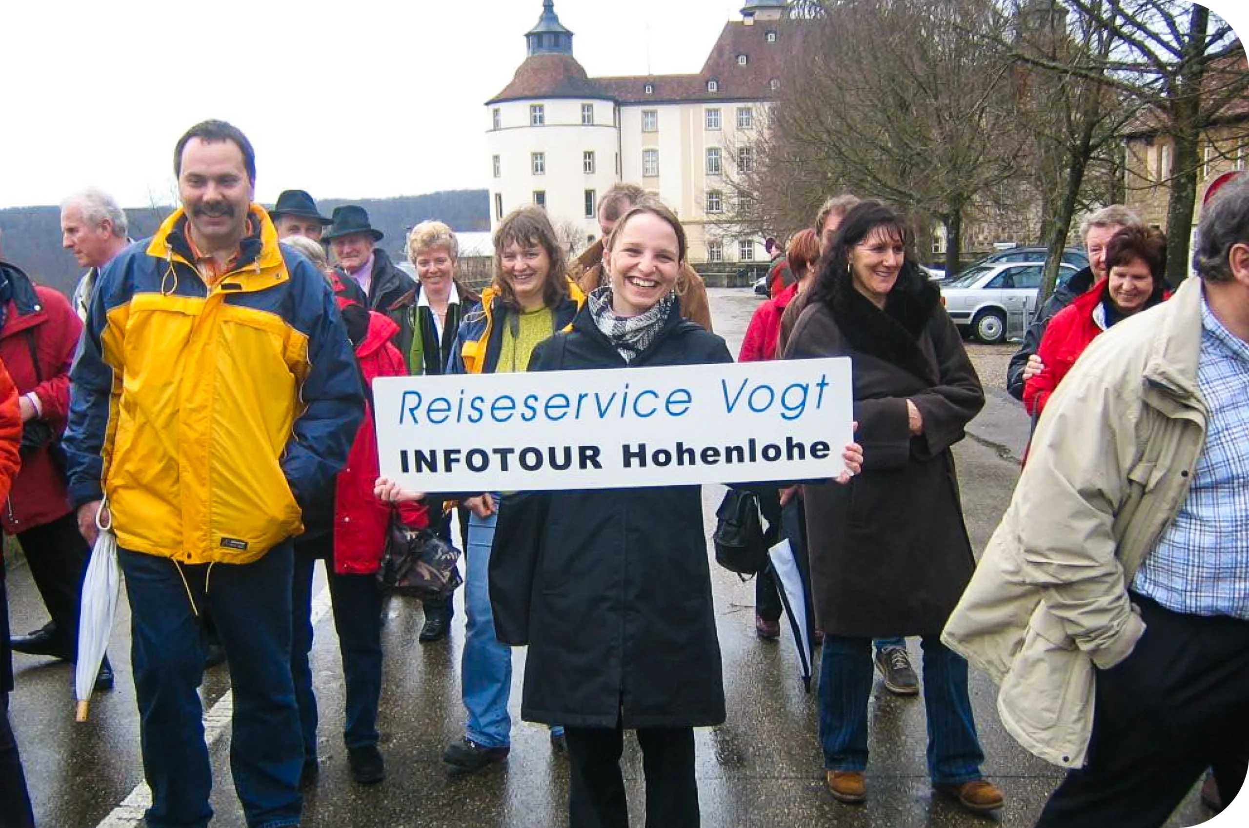 Reisegruppe in Hohenlohe. Lachende Frau mit großem Schild "ReiseService VOGT Infotour Hohenlohe"