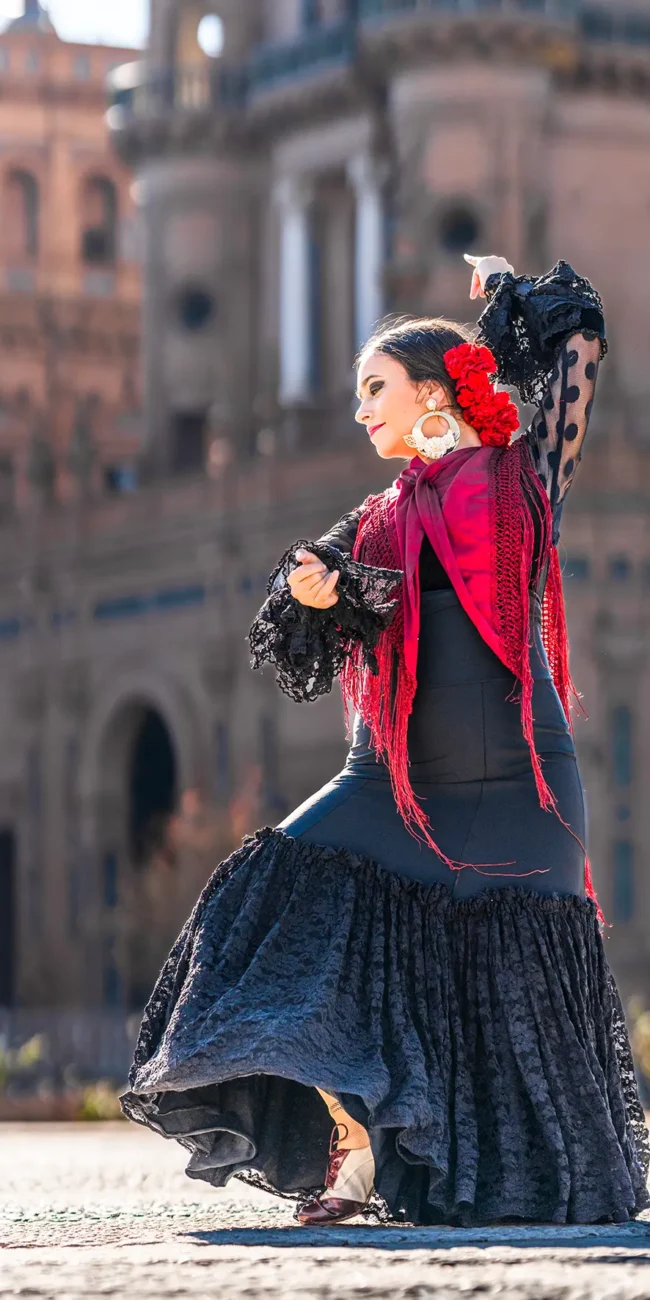 Eine Flamenco-Tänzerin trägt ein schwarzes Spitzenkleid mit Rüschen, große Ohrringe und rote Accessoires.