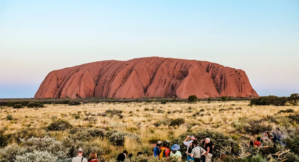 Eine Reisegruppe fotografiert den Ayers Rock in Australien bei Sonnenaufgang