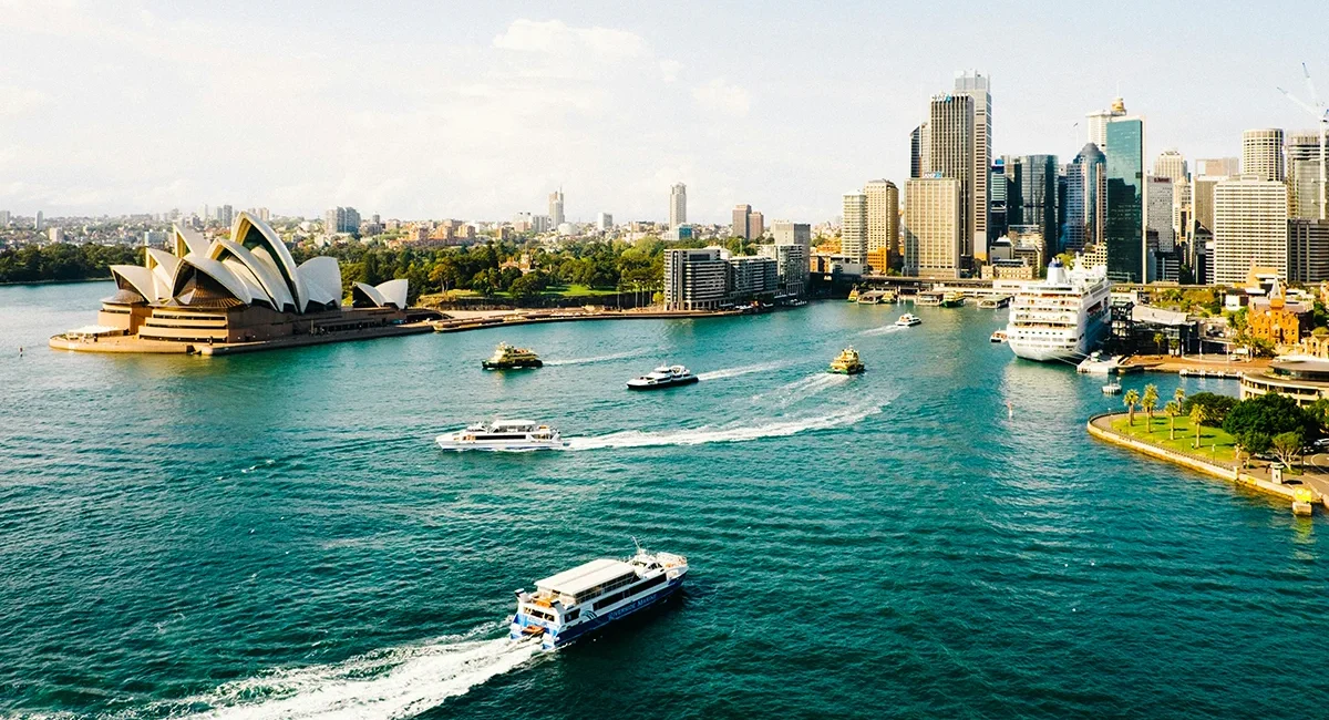 Ein Boot fährt auf den Hafen Sydneys in Australien zu, wo man im Hintergrund das berühmte Opernhaus sehen kann.