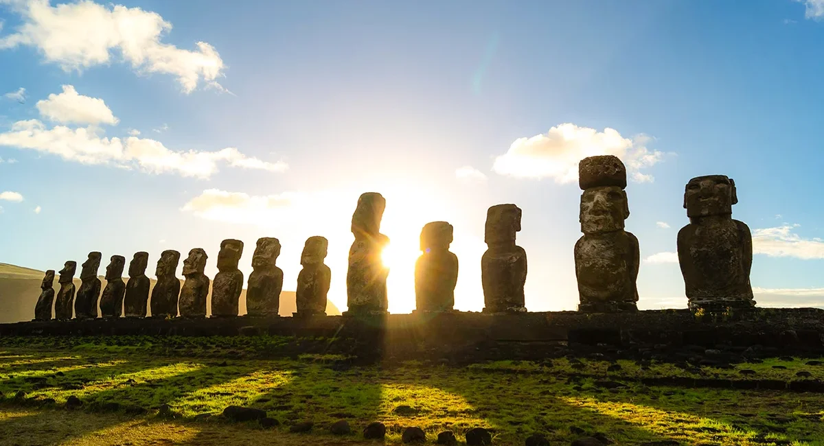 Sonnenaufgang auf den Osterinseln in Chile. Die Sonne scheint durch eine Reihe Moai, die monumentalen Statuen, die dort auf der Insel zu finden sind.