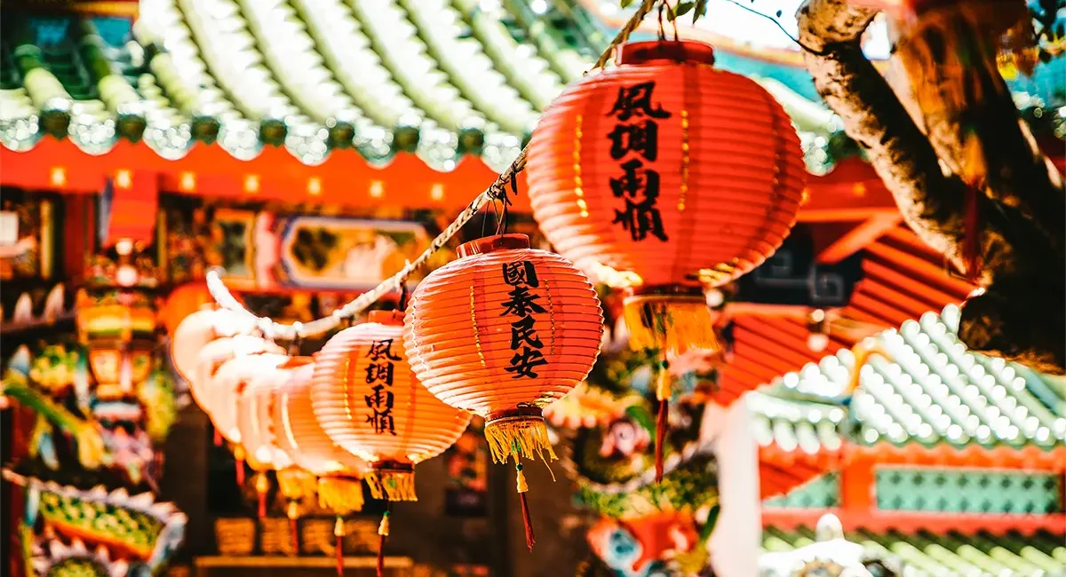 Rote chinesiche Lampions mit chinesischen Schriftzug zwischen traditionell gestalteten Gebäuden