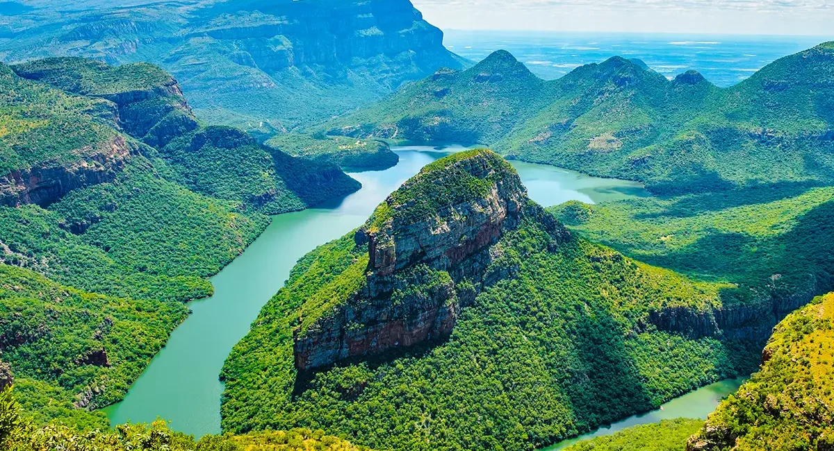 Der smaragdgrüne Blyde River Canyon in Südafrika, umgeben von grünen Felsformationen und weiter Landschaft im Hintergrund.