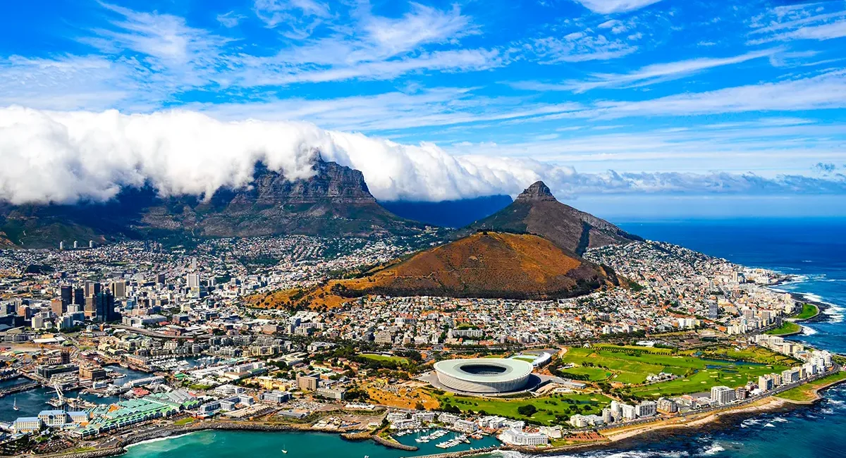 Weitläufiger Blick auf Kapstadt, eingebettet zwischen dem Atlantik und dem markanten Tafelberg, der von einer Wolkendecke umhüllt wird.