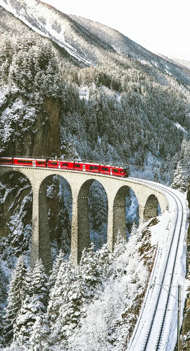 Die rote Glacier Express Bahn überquert im Winter den berühmten, schneebedeckten Landwasserviadukt in der Schweiz.