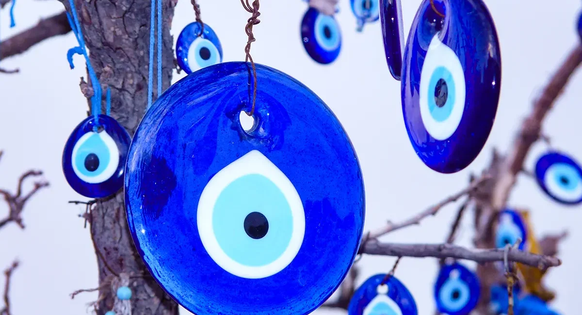 Mehrere blaue, augenförmige Nazar-Amulette, auch Auge der Fatima genannt, hängen an den Ästen eines Baumes.
