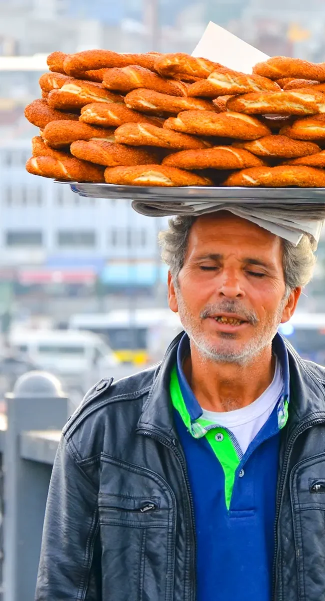 Ein einheimischer Verkäufer, der die traditionellen türkischen Sesamkringel, Simit genannt, auf einem Tablett auf dem Kopf trägt.