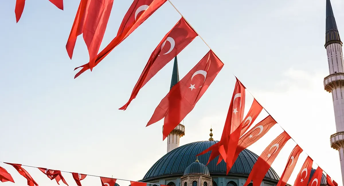 Zahlreiche türkische Flaggen sind über einer großen Moschee mit Kuppel und Minaretten aufgehängt.