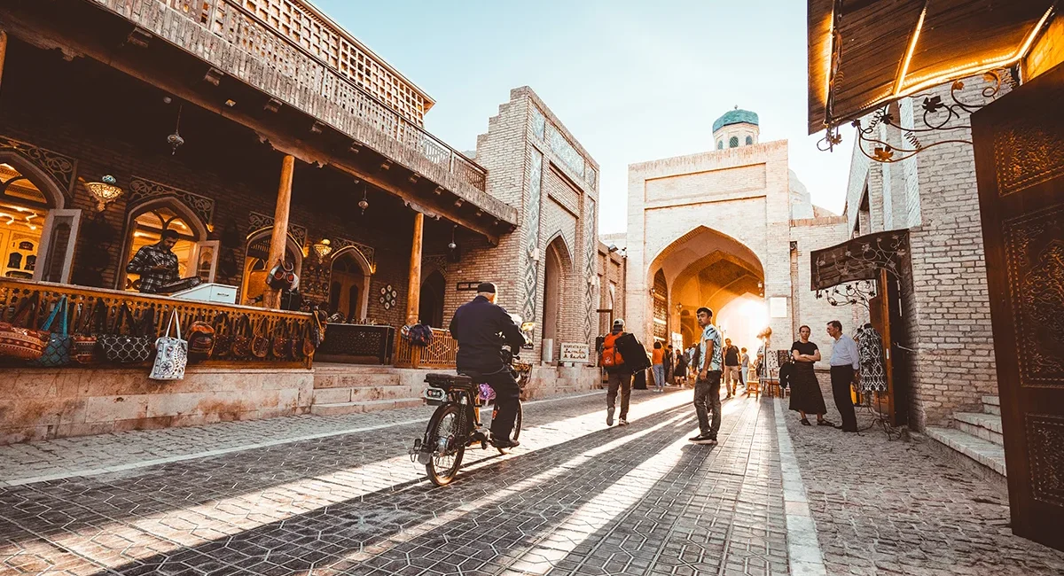 Eine lebendige Straße in der Altstadt von Buchara in Usbekistan mit historischen Gebäuden und dem Stadttor.