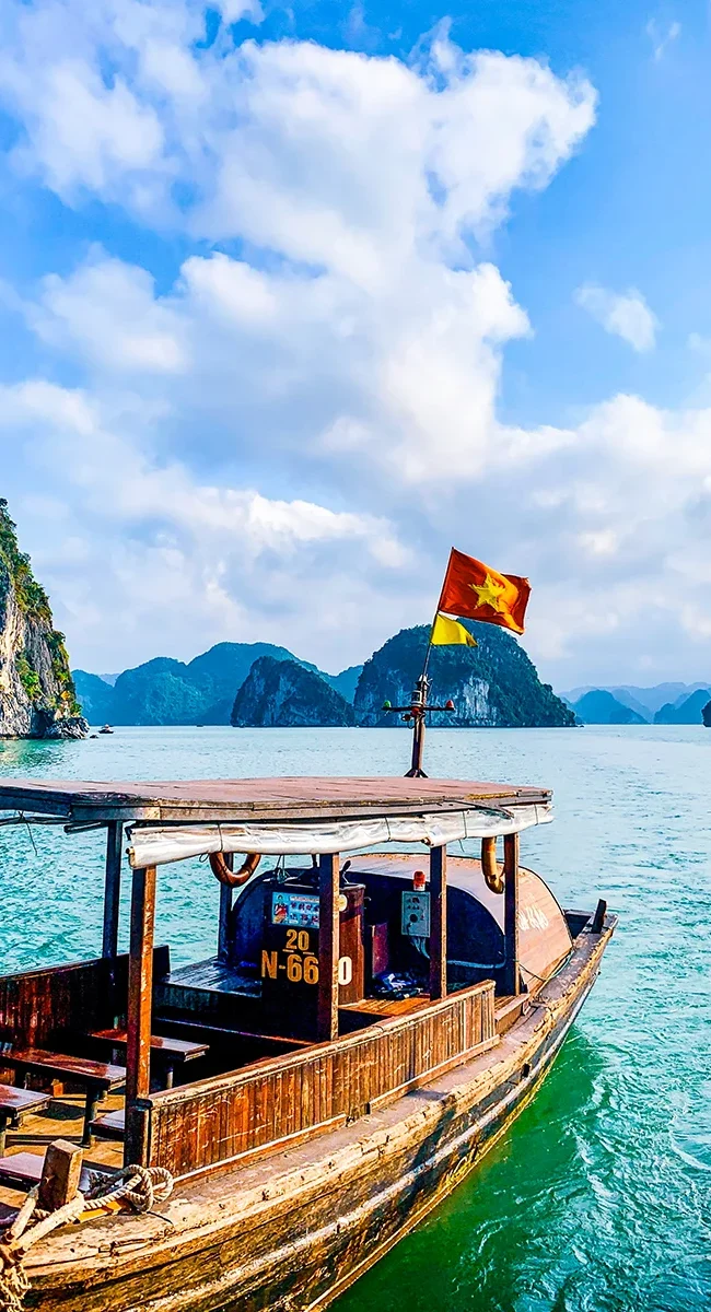 Ein traditionelles Holzboot in der vietnamesischen Halong Bucht mit smaragdgrünem Wasser und vielen Kalksteininseln im Hintergrund.