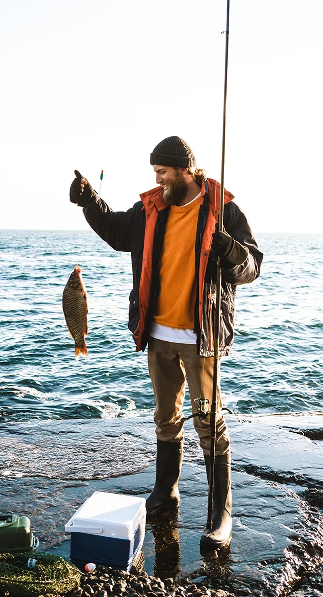Ein Angler steht an der Küste von Dänemark und hat einen Fisch gefangen.