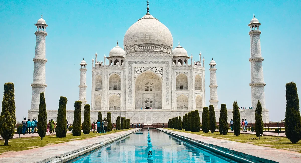 Das Taj Mahal, ein berühmtes Mausoleum aus weißem Marmor in Agra, Indien, das sich symmetrisch in einem davor liegenden, langen Wasserbecken spiegelt.