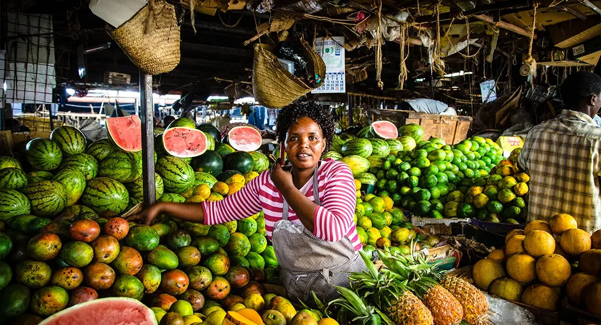 Eine kenianische Frau, die an einem Obststand in Nairobi, Kenia, steht und Melonen und anderes Obst verkauft.