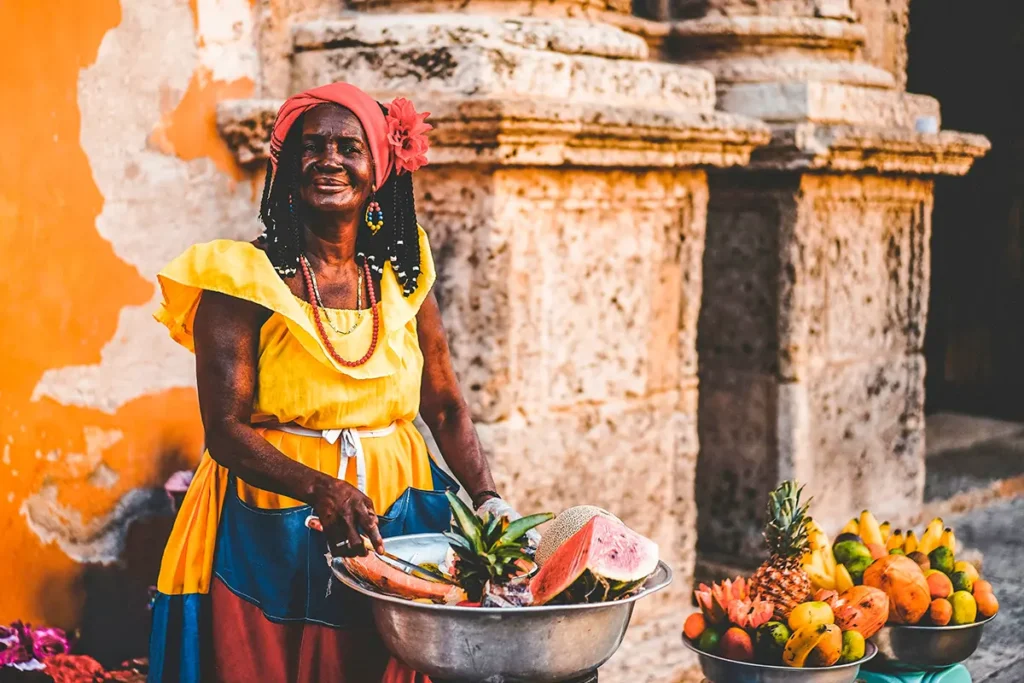 Eine afrokolumbianische Frau in farbenfroher traditioneller Kleidung, die in Kolumbien, an einem Stand frische tropische Früchte verkauft.