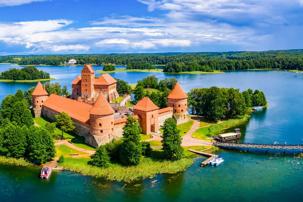 Die Inselburg Trakai in Litauen, die auf einer Insel inmitten des tiefblauen Galvė-Sees liegt und über einen langen Holzsteg mit dem bewaldeten Festland verbunden ist.