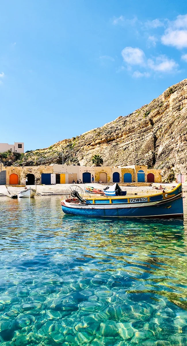 Eine natürliche Lagune auf Malta mit kristallklarem Wasser, hohen Klippen und kleinen bunten Fischerhütten.