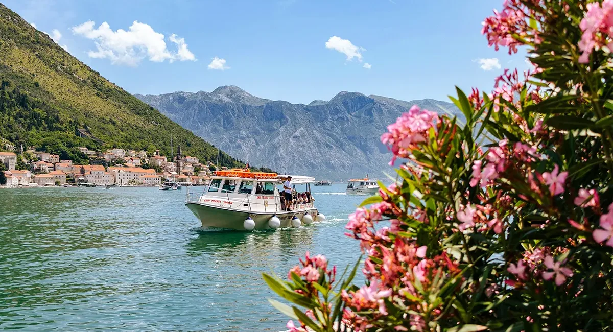 Die malerische Bucht von Kotor in Montenegro, wo ein Ausflugsboot vor der Kulisse der historischen Stadt Perast und steiler Berge über das Wasser gleitet.