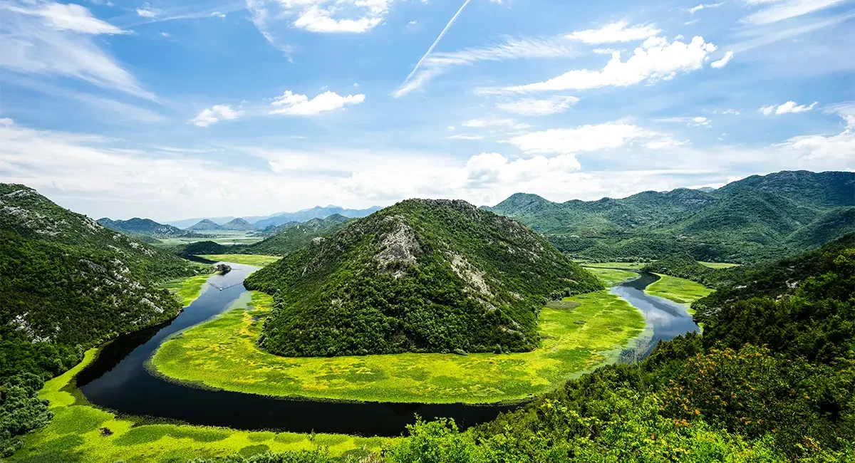 Die berühmte, hufeisenförmige Flussschleife, die sich durch üppig grüne Hügel im Nationalpark Skutarisee in Montenegro schlängelt.