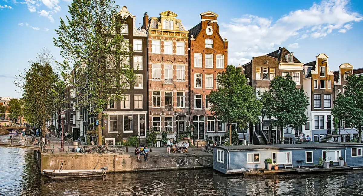 Eine Häuserreihe in Amsterdam direkt am Kanal, geprägt von den typischen schmalen Giebelhäusern.