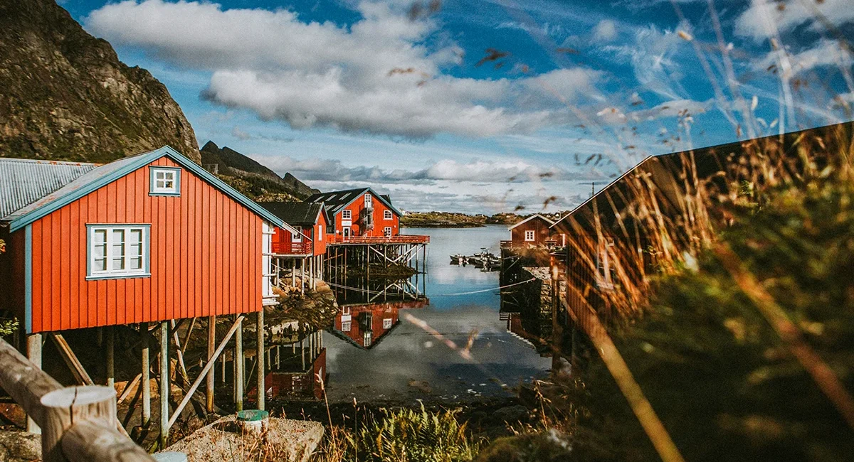 Auf den norwegischen Lofoten steht ein traditionelles Fischerdorf mit roten Hütten auf Stelzen in einer ruhigen Bucht.