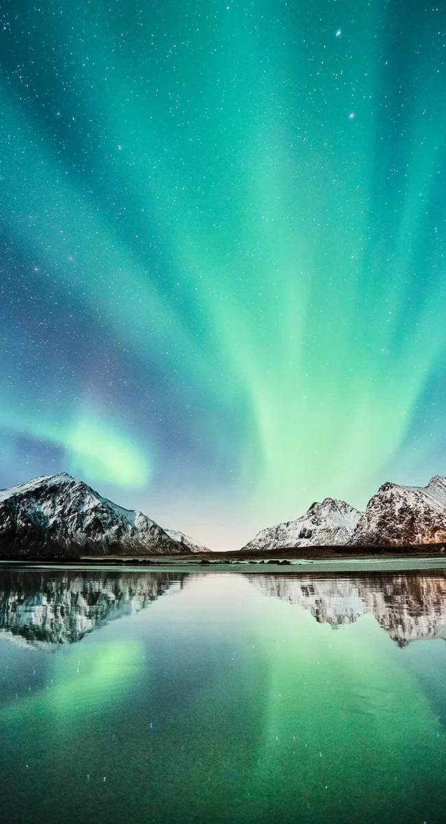 Nordlichter leuchten über schneebedeckten Bergen und spiegeln sich in einem stillen See in Norwegen.