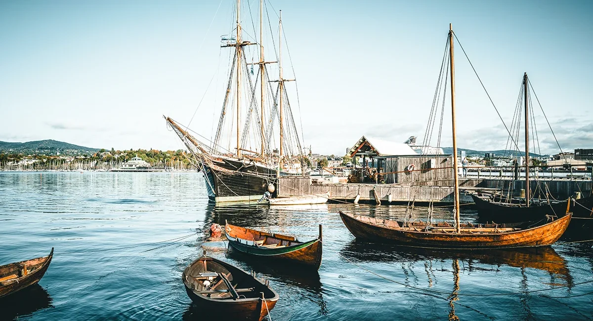 Mehrere traditionelle Holzboote, darunter ein großes Segelschiff, die an einem sonnigen Tag im Hafen von Oslo, Norwegen liegen.