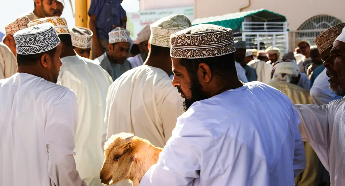 Omanische Männer, die traditionelle Kleidung tragen, während sie an einem Ziegenmarkt teilnehmen.