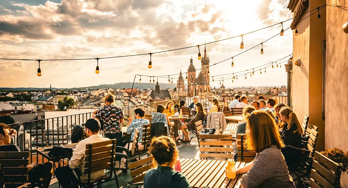 Von einer Dachterrasse hat man einen weiten Blick über Krakau, während zahlreiche Menschen an den Tischen sitzen und etwas trinken.