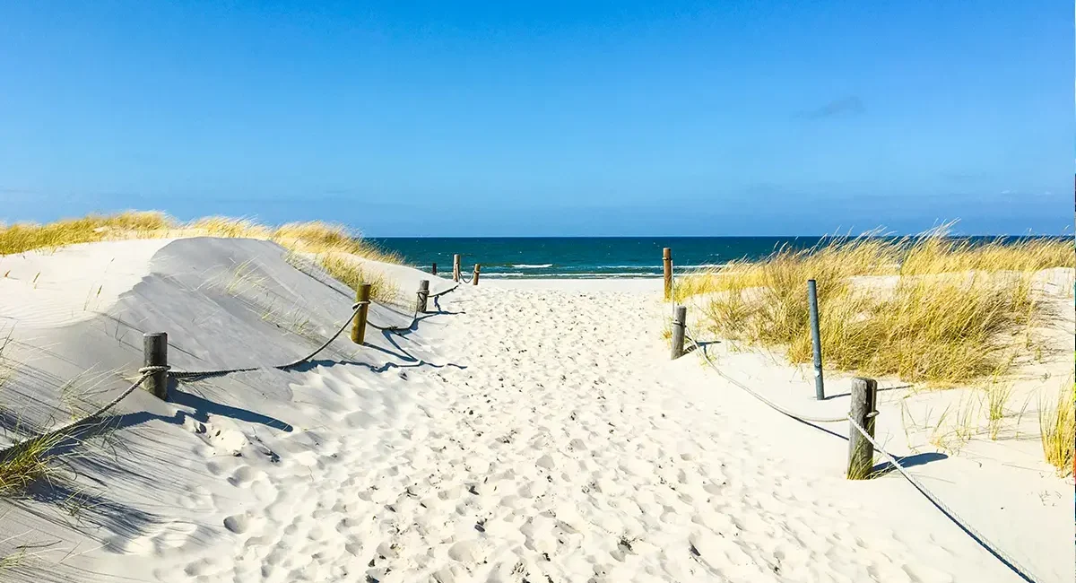 Ein Sandstrand an der polnischen Ostsee mit Dünen und einem Weg zum Wasser.