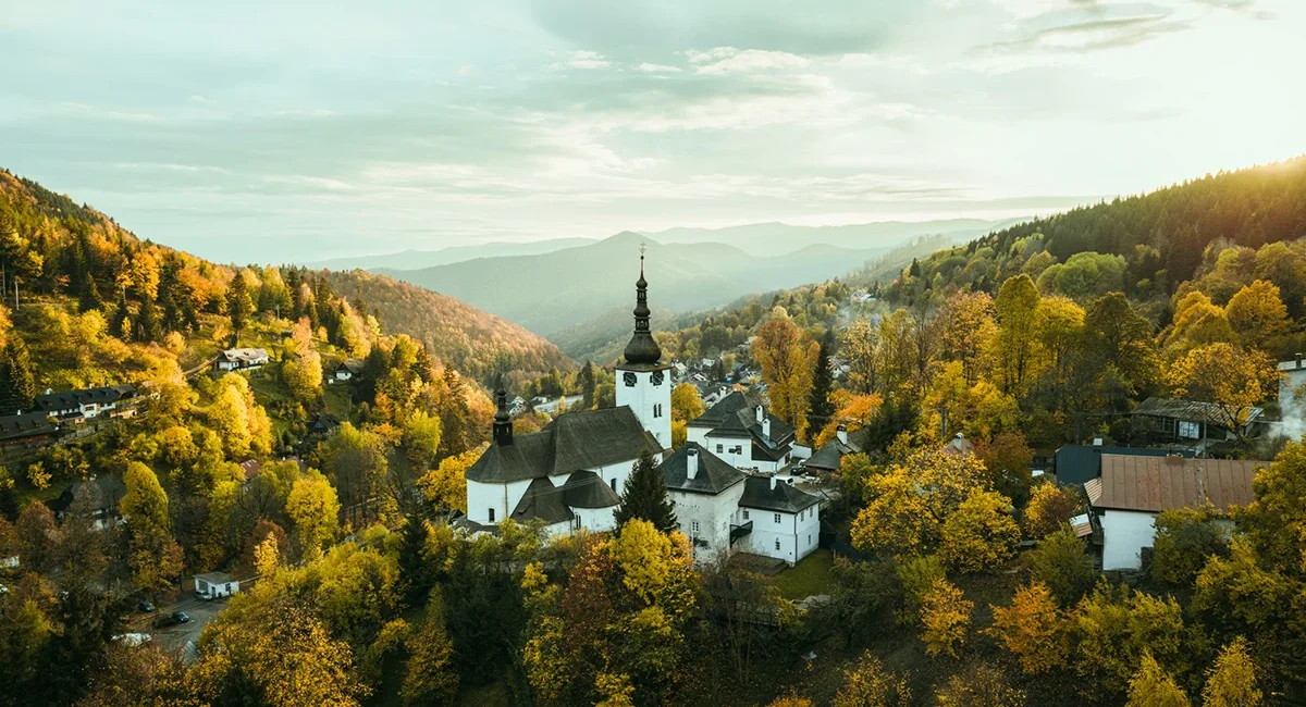 Das historische Bergbaudorf Špania Dolina in der Slowakei, eingebettet in ein malerisches Tal mit einer markanten Kirche und umgeben von herbstlich gefärbten Wäldern.