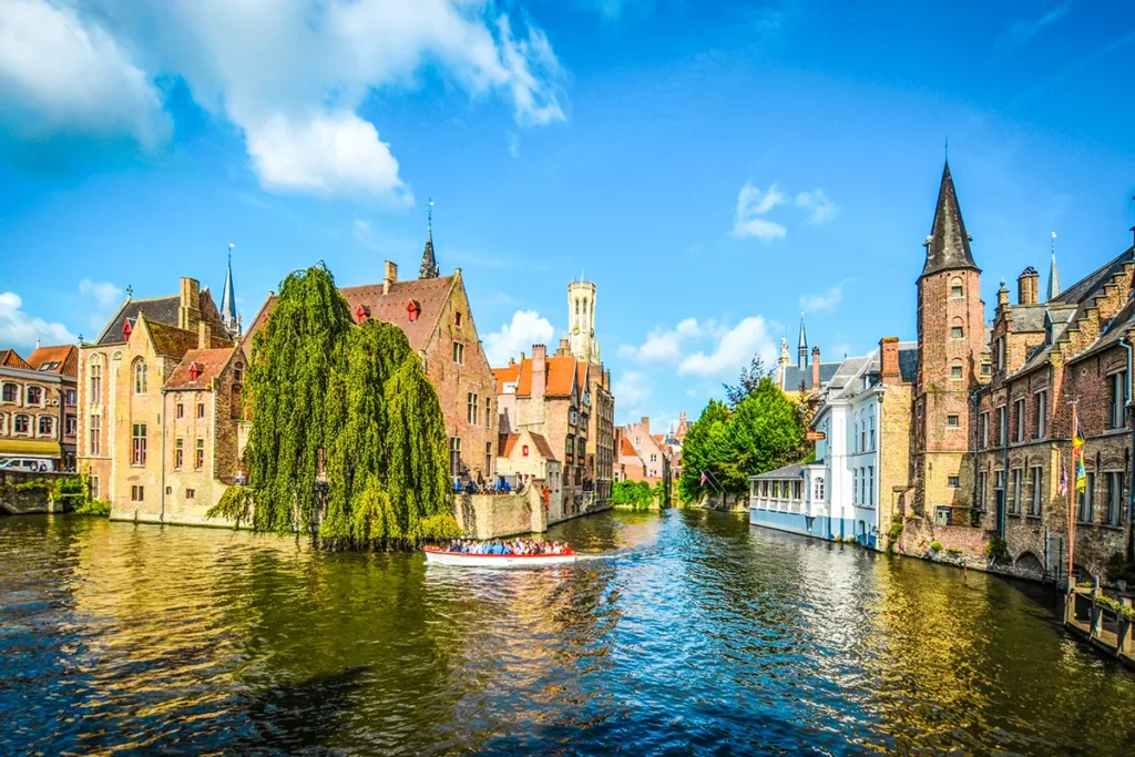 Der Rozenhoedkaai in der mittelalterlichen Altstadt von Brüggein Belgien, wo historische Backsteingebäude und der markante Belfried das Ufer eines Kanals säumen, wo gerade eine Grachtenfahrt stattfindet.