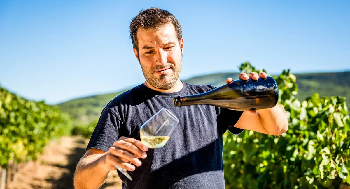 Ein belgischer Winzer steht in den Weinbergen und schenkt ein Glas Wein ein.