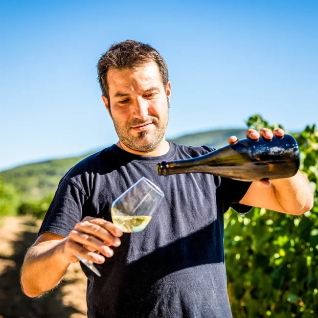 Ein belgischer Winzer steht in den Weinbergen und schenkt ein Glas Wein ein.