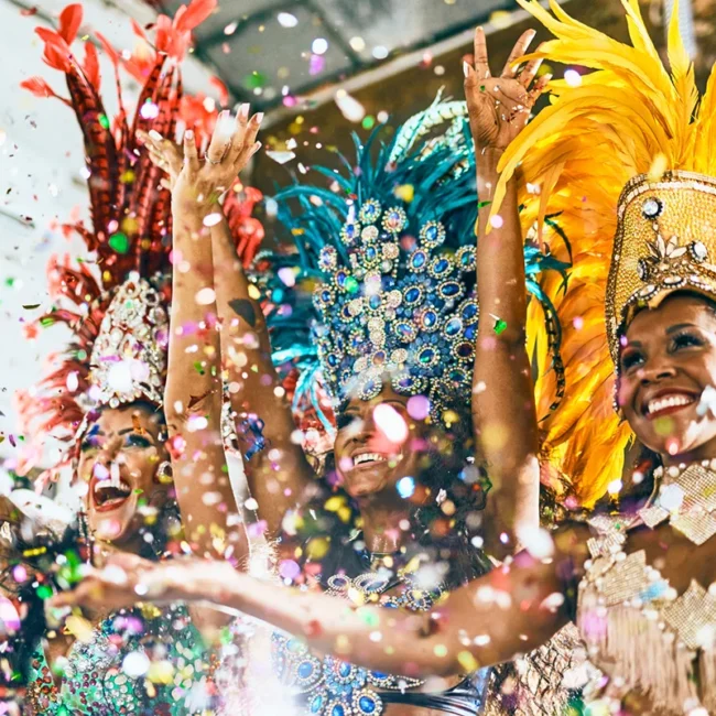 Drei bunt kostümierte Samba-Tänzerinnen beim brasilianischen Karneval mit viel Konfetti im Vordergrund.