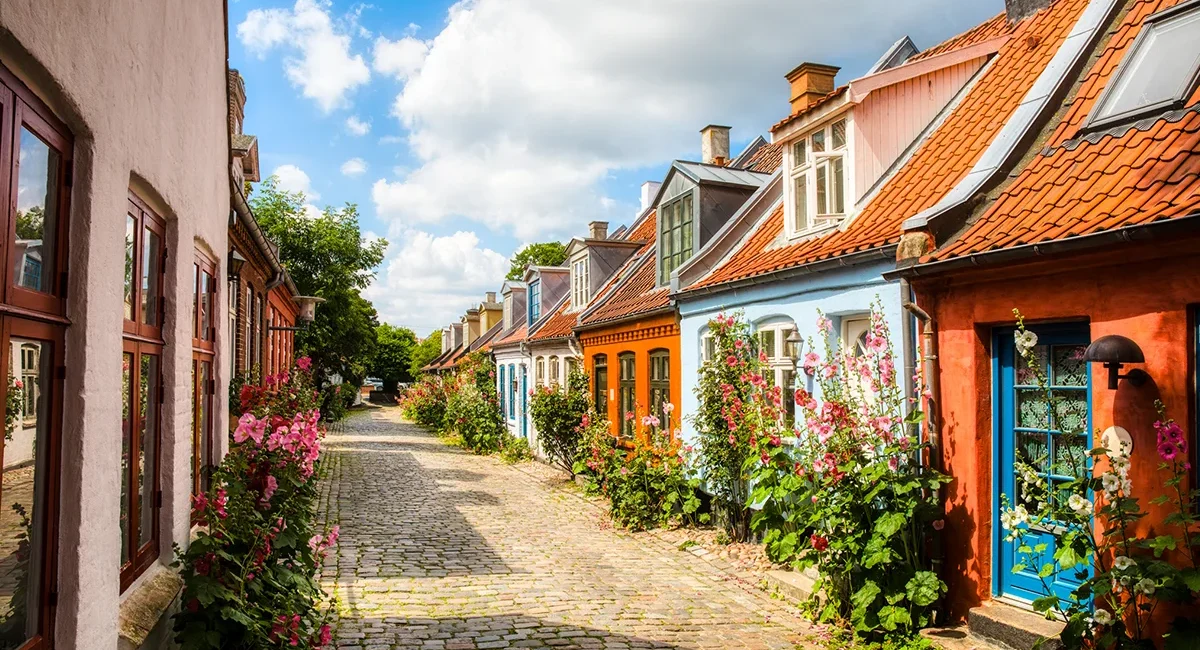 Eine schmale Gasse mit Kopfsteinpflaster in Aarhus, Dänemark mit kleinen bunten Häusern und Blumen.