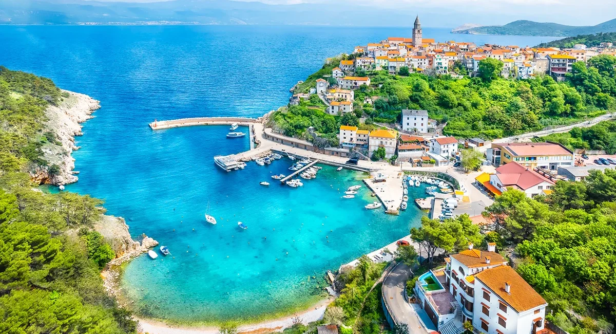 Der Ort Vrbnik auf der kroatischen Insel Krk, mit Blick auf seinen türkisfarbenen Hafen und die umliegende Adria.