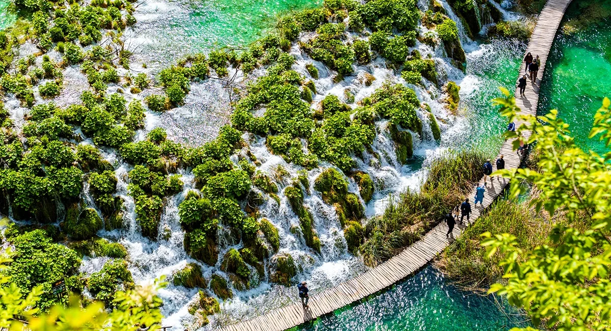 Die türkisfarbenen Seen und Wasserfälle im kroatischen Nationalpark Plitvicer Seen, die von üppiger Vegetation umgeben sind und über einen gewundenen Holzsteg von Besuchern erkundet werden.