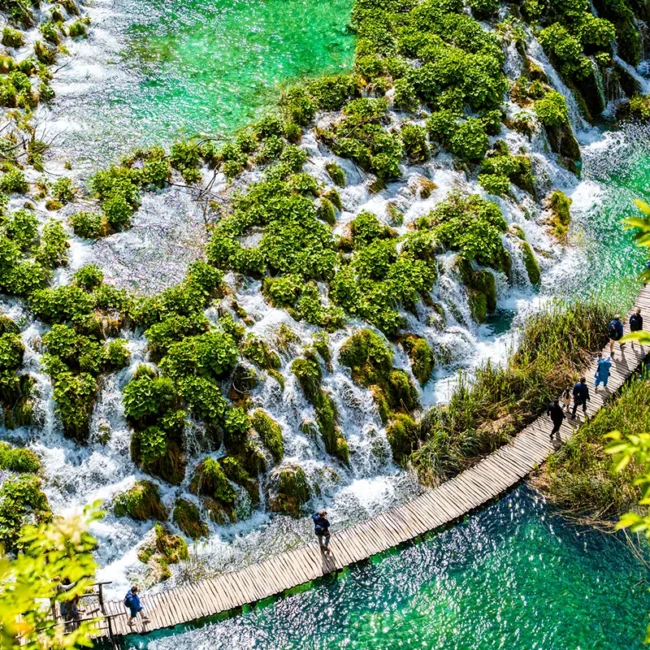 Die türkisfarbenen Seen und Wasserfälle im kroatischen Nationalpark Plitvicer Seen, die von üppiger Vegetation umgeben sind und über einen gewundenen Holzsteg von Besuchern erkundet werden.
