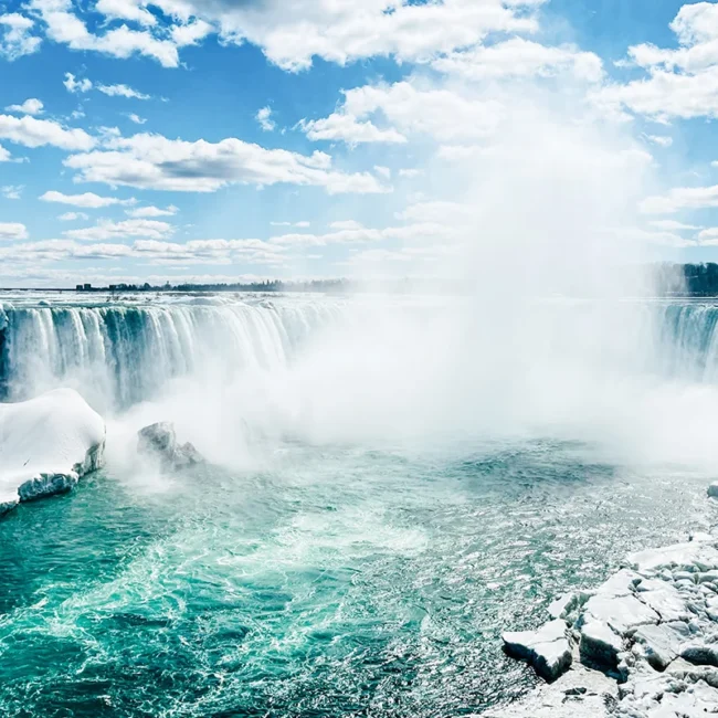 Die teilweise vereisten Niagarafälle inmitten einer verschneiten Winterlandschaft unter einem strahlend blauen, leicht bewölkten Himmel in Ostkanada.