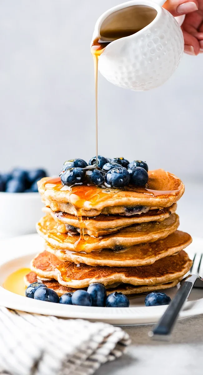 Ein Turm von Pancakes, die mit Blaubeeren und Ahornsirup garniert werden.