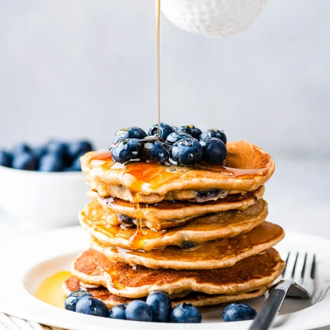 Ein Turm von Pancakes, die mit Blaubeeren und Ahornsirup garniert werden.