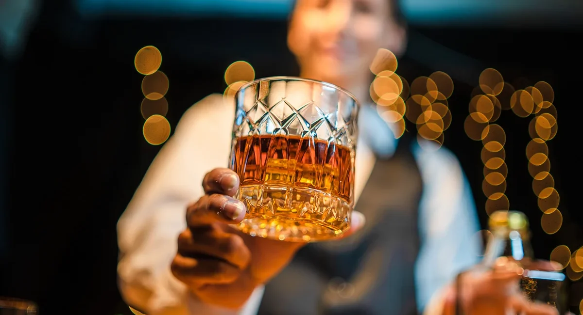 Ein Glas schottischer Whisky mit einem Barkeeper im Hintergrund.