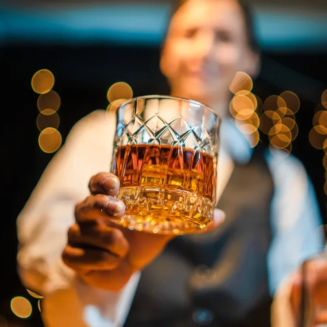Ein Glas schottischer Whisky mit einem Barkeeper im Hintergrund.