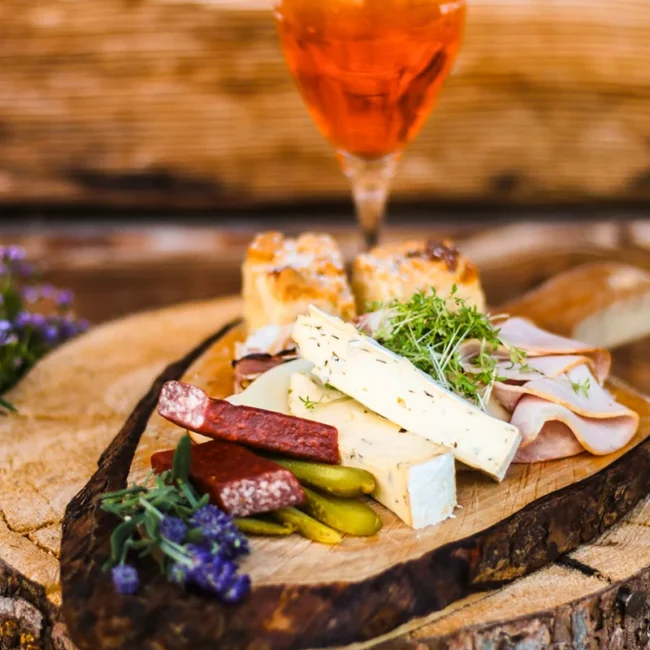 Ein Vesperbrett mit frischem Käse, Wust, Kuchen und einem Glas Aperol in Südtirol.