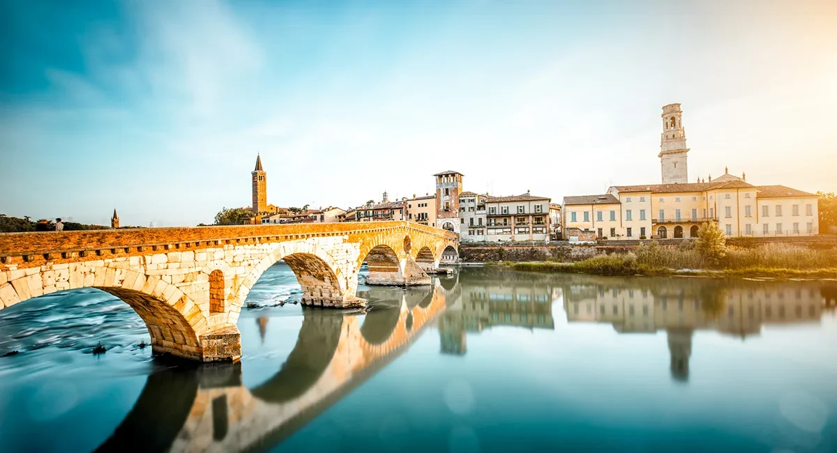 Die historische römische Bogenbrücke Ponte Pietra, die bei tiefstehender Sonne den Fluss Etsch in der italienischen Stadt Verona überspannt.