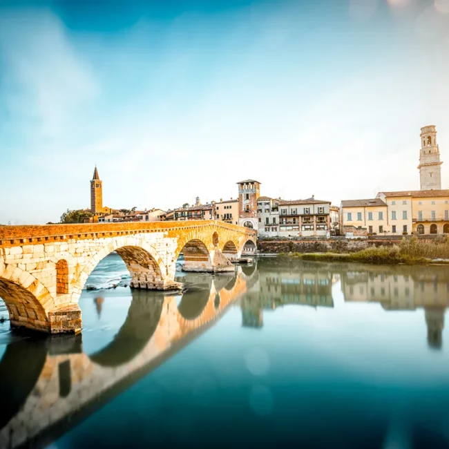 Die historische römische Bogenbrücke Ponte Pietra, die bei tiefstehender Sonne den Fluss Etsch in der italienischen Stadt Verona überspannt.
