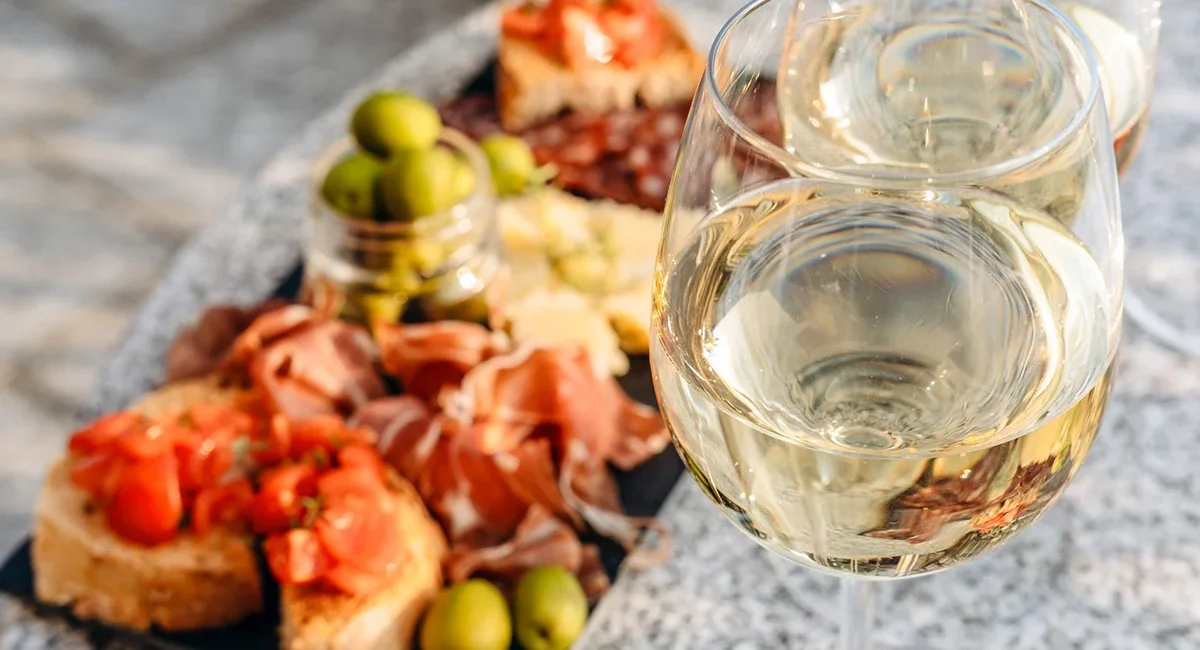 Vesper mit Baguette, Tomaten und Schinken auf einem Teller angerichtet, dazu Wein