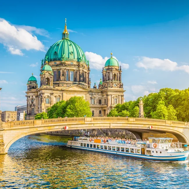 Der majestätische Berliner Dom mit seiner markanten grünen Kuppel hinter der Schlossbrücke, während ein Ausflugsschiff auf der Spree vorbeifährt.